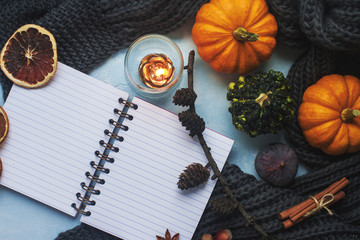 Cozy autumn background, notebook, decorative pumpkins, dried oranges, candle, nuts, cinnamon and autumn leaves
