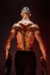 Fototapeta na wymiar The back view of torso of attractive male body builder with dumbbells on dark smoky background.