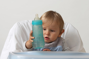 blond baby grabs her bottle to eat