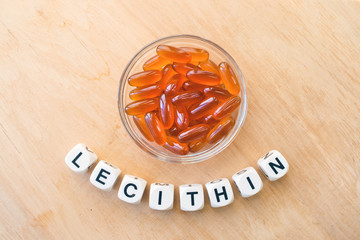 Lecithin gel pills in a round glass bowl and with the word Lecetin from the letters of cubes on a light wooden background. Soy and sunflower lecithin benefits for skin, digestion, lower cholesterol.
