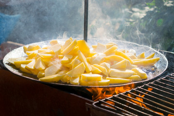 Cooking roasted French Fried potatoes for barbecue picnic. Fried bbq potatoes in a large frying pan on an open fire with smoke. Crispy Oven Baked French Fries at the stake