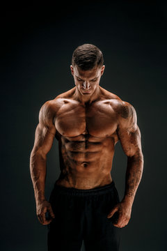 Very brawny guy bodybuilder posing. Beautiful sporty guy male power. Fitness muscled man in studio. Dark background.