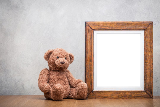 Retro oak wooden photo frame blank and Teddy Bear toy on table front concrete wall background. Vintage old style filtered photography