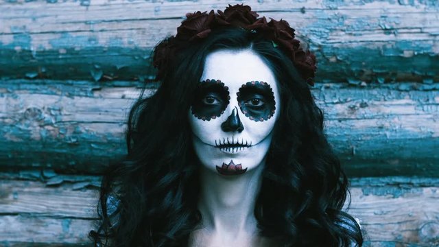 The Mexican Day of the Dead. The portrait of young woman with frightening make-up for Halloween on the background of wooden wall. 4K