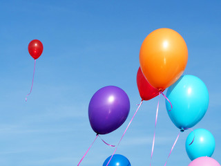 Multicolored inflatable balloons filled with helium against the blue sky, one red balloon flew away