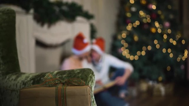 Beautiful couple celebrating Christmas. Lovers celebrate the New Year at home. Consider an album of photos. Blurred background. Xmas tree with bright colored lights. red and white hats.