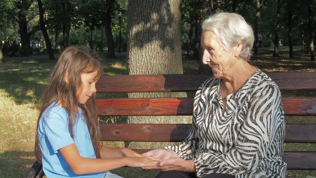 The child is stroking the hands of his grandmother. Little girl with an elderly grandmother on a bench in the park.