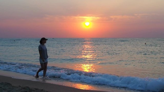 A girl at dawn is walking along the seashore. A happy girl at dawn is walking along the beach.