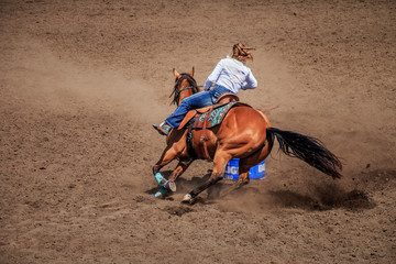Cowgirl riding her horse around a barrel in a barrel racing competition. The horse is kicking up a...