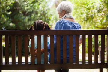 Rear view of granddaughter and grandmother sitting on wooden