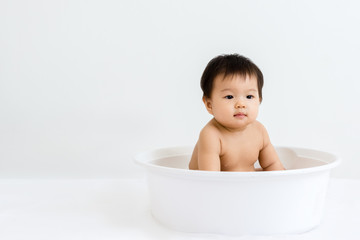 Portrait of adorable baby sitting in the basin for shower, indoors