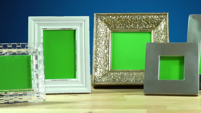 Row of various photo frames with green screen on elegant table interiors display, panning across close up.