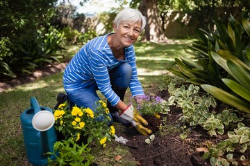 Portrait of smiling senior woman kneeling while planting flowers - Powered by Adobe