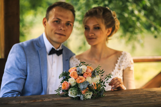 Young groom and beautiful bride with a wedding bouquet sitting in the arbor. Young family in wedding day.