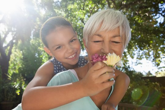 Grandmother Smelling Flowers While Piggybacking Granddaughter