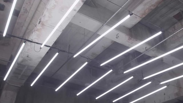 Slow motion shot of white fluorescent lighting turn on and off in the dark in industrial building. Many lighting neon lights blinking and flashing on the ceiling.