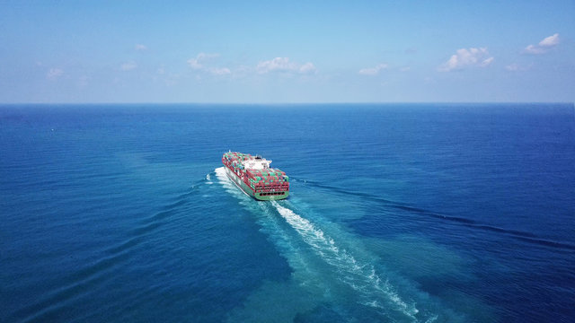 Huge large mega container ship sails on open water fully loaded with containers and cargo - aerial view