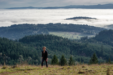 Fototapeta na wymiar A woman hikes up a hill overlooking a wide valley covered in low clouds.