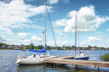 Yachts on lake on clear summer day. White yachts or boats against blue sky with clouds