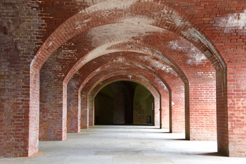 Old fort brick walkway, decrepit falling apart, stained. Dark shadowed hallway at end of the corridor.