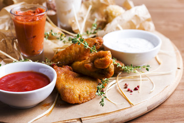 Spicy baked chicken wings with appetizers and sauces on round wooden Board