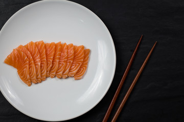 raw salmon sashimi on a white plate on black background