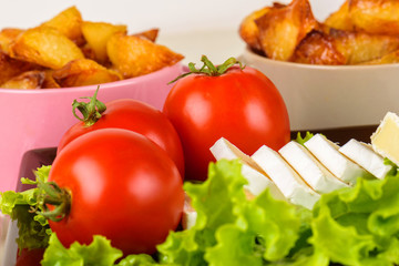 Breakfast from cheese, tomatoes, potatoes and all-over salad on a wooden table closeup.