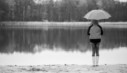 eine Frau steht bei Regenwetter mit einem Regenschirm an einem See