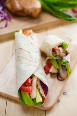 tortilla wrap with grilled chicken,avocado,tomato and lettuce on wooden board