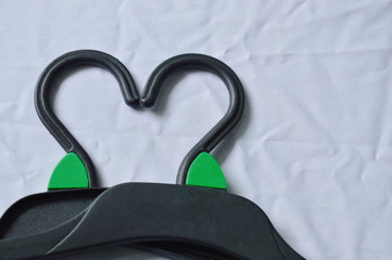 black plastic clothes hanger arranging heart shape on white fabric background
