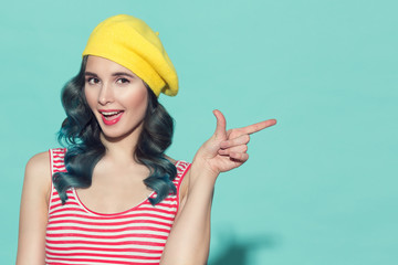 Beautiful woman in a yellow beret pointing finger on copyspace. On a blue background.