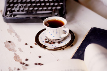 Old metal typewriter, covered in dust and rust. Cup of coffee on the table. The atmosphere of comfort and creativity. Retro