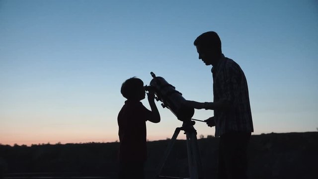 Anonymous man with little boy looking through telescope in twilight.
