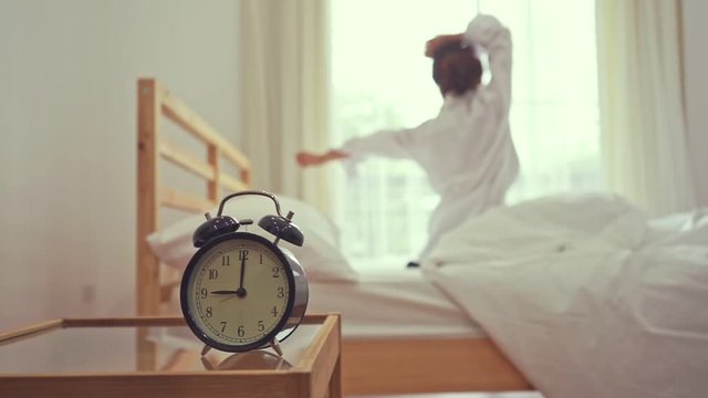 Closeup alarm clock, Young asian woman wake up in the morning and sitting on bed at mirror door side relaxing in holiday with sunlight, Vintage 
