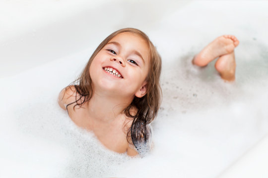 Happy little child girl is taking a bath with a foam