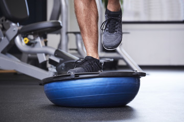 Dude jogging on bosu ball in gym, close up