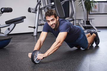 Fototapeta na wymiar Sporty guy crunching abs with gym wheel, portrait