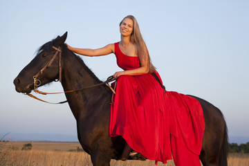 Happy young woman in a red dress riding a horse smiling looking at the camera