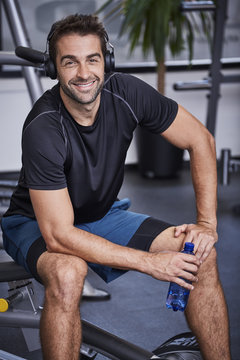 Smiling guy in gym with headphones and water bottle, portrait