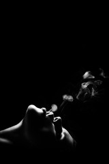 beautiful young woman smoking on black background with copy space, monochrome