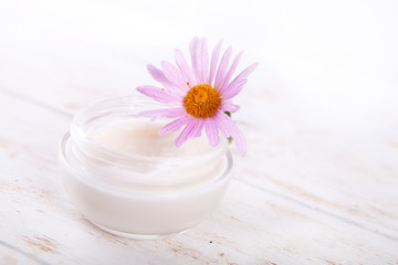 Fototapeta na wymiar face-cream and flower on a white wooden background. natural organic cosmetic facial. space for text