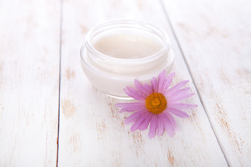 Fototapeta na wymiar pot of moisturizing face cream and beautiful flower on a white wooden background. natural organic cosmetic facial. Close up