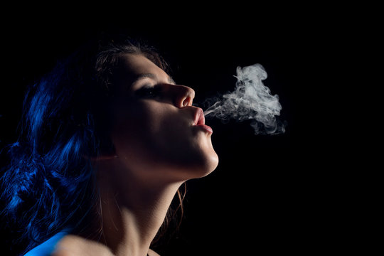beautiful young woman smoking on black background with copy space