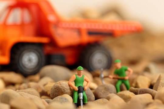 Miniature construction workers on gravel with tipper truck in the background