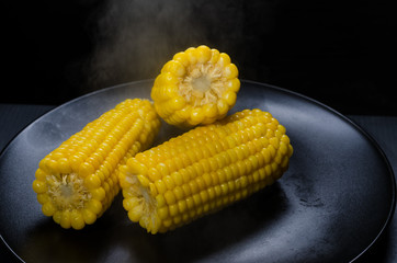 corn with steam on a black plate.