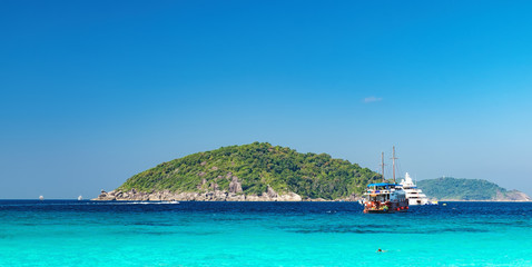 Obraz premium View from the beach to the crystal blue water of the Andaman Sea and Similan Island, Thailand. Tourist boats and the island on the horizon, sea cruise in tropical waters