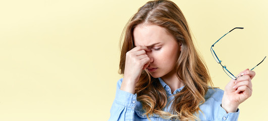 Beautiful teenager girl with ginger hair and freckles holding reading glasses, having headache and...