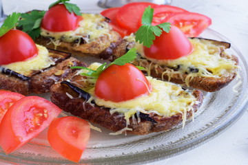 Toasts with aubergine, cheese and tomato on a glass plate.