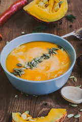 Roasted pumpkin soup with cream and pumpkin seeds on wooden background.