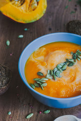 Roasted pumpkin soup with cream and pumpkin seeds on wooden background.
